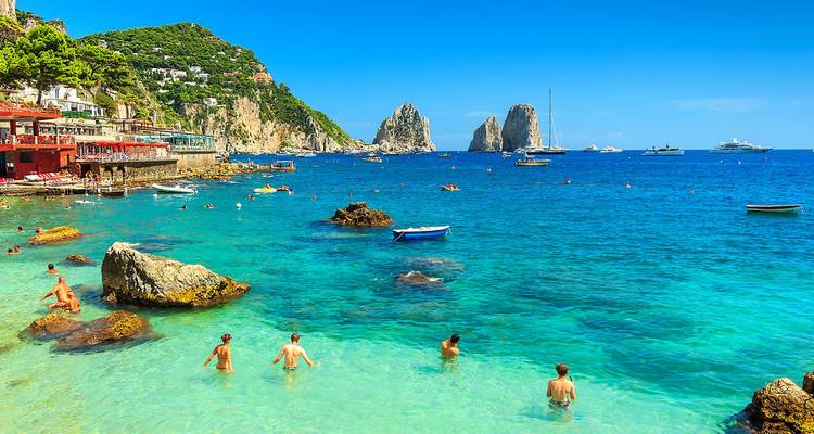 Zwemmers genieten van kristalhelder turquoise water bij Capri met uitzicht op de Faraglioni-rotsen en jachten.
