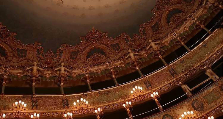 Techo interior dorado y ornamentado de la histórica ópera La Fenice de Venecia iluminado por candelabros.