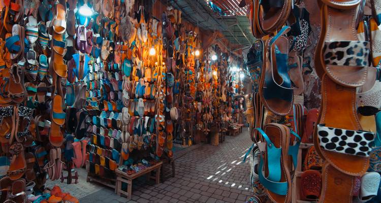 Smalle souk doorgang omzoomd met hangende leren sandalen in talloze kleuren verlicht door lampen.