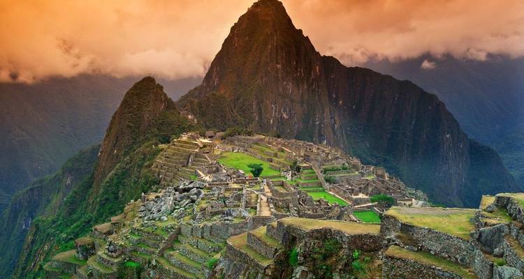 Vue emblématique des ruines de Machu Picchu perchées sur un flanc de montagne avec des nuages dramatiques de lever de soleil et des terrasses vertes