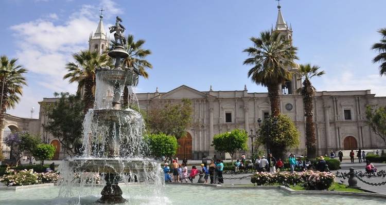 Grand colonial basilica overlooking a bustling fountain-filled main square with palm trees and tourists