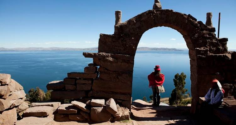 Stone archway framing panoramic blue waters of Lake Titicaca with a traveller in red standing at the edge