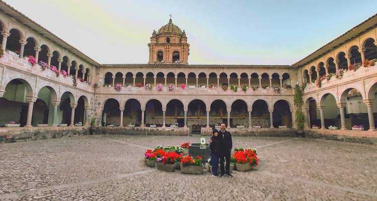 Pareja de pie en el patio floral del monasterio Qorikancha en Cusco con campanario arriba.