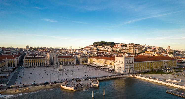 Drone view of Lisbon’s Praça do Comércio and waterfront bathed in late afternoon light.
