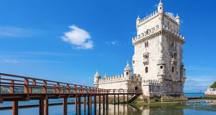 Iconic Belém Tower rising from the Tagus River with wooden walkway and bright blue sky.