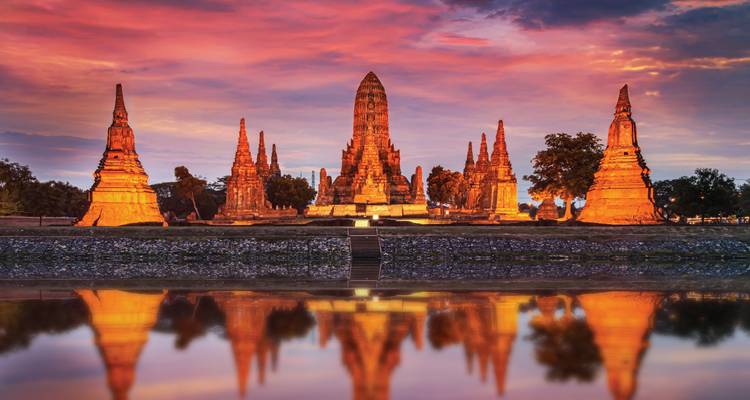Wat Chaiwatthanaram verlicht in de schemering perfect weerspiegeld in het stille rivierwater onder een levendige hemel