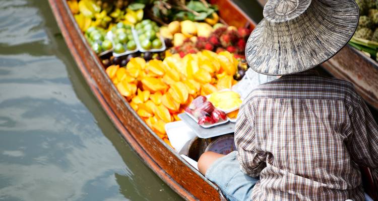 Verkoper met strohoed die een houten boot vol kleurrijke tropische vruchten peddelt op een kanaal van een drijvende markt
