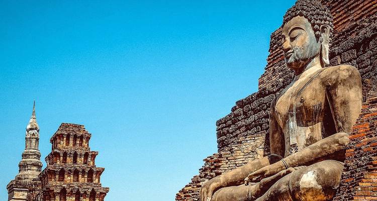 Oud zittend Boeddhabeeld en bakstenen stupa's van een historisch tempelcomplex tegen een diepblauwe hemel.