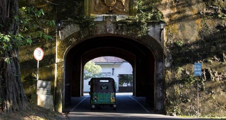 Groene tuk-tuk die een met mos bedekte stenen poorttunnel verlaat binnen een oud fort onder gevlekt zonlicht.