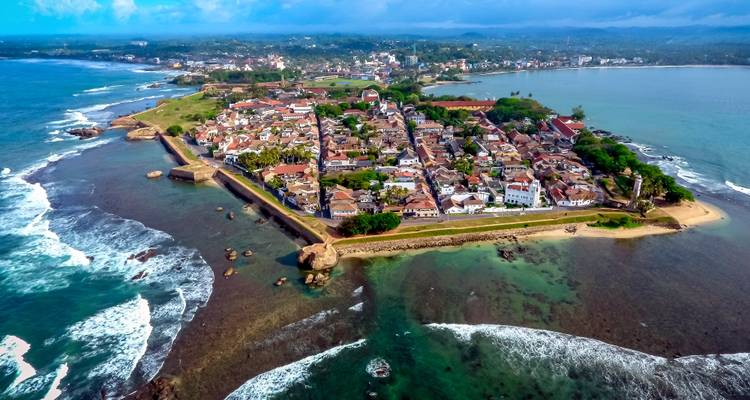 Dronebeeld van het Galle Fort-schiereiland omringd door turquoise zeeën en brekende golven.