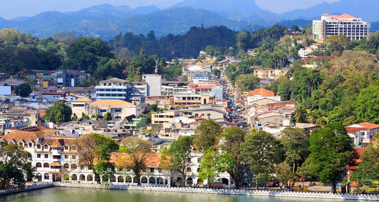Un colorido paisaje urbano de montaña en Kandy con un lago en primer plano y montañas distantes.