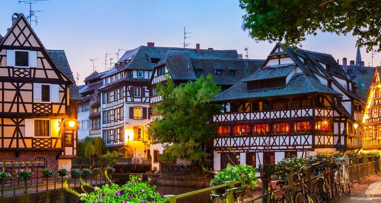 Abendszene von Straßburgs La Petite France mit Fachwerkhäusern, die sich im Kanal spiegeln, und aufgereihten Fahrrädern.