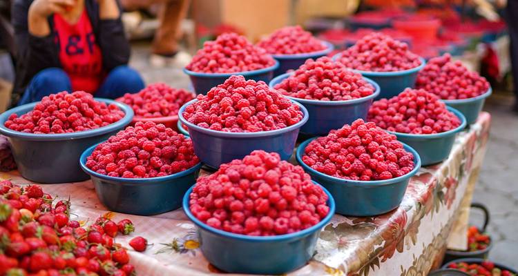 Tazones rebosantes de frambuesas frescas sobre mesa de mercado estampada en bazar de Asia Central