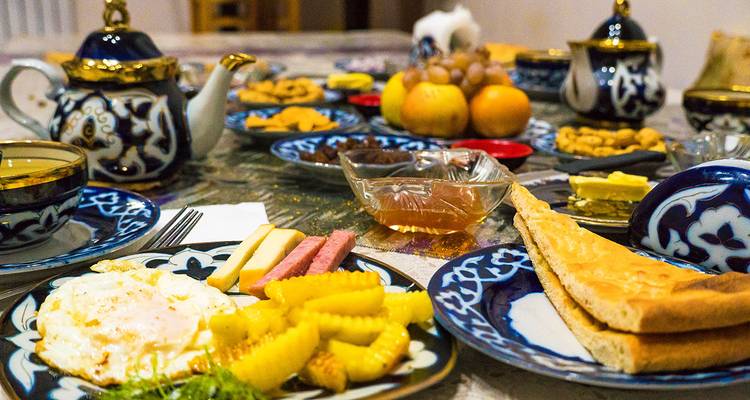 Mesa de desayuno uzbeko tradicional con platos azules ornamentados, huevos, pan y dulces