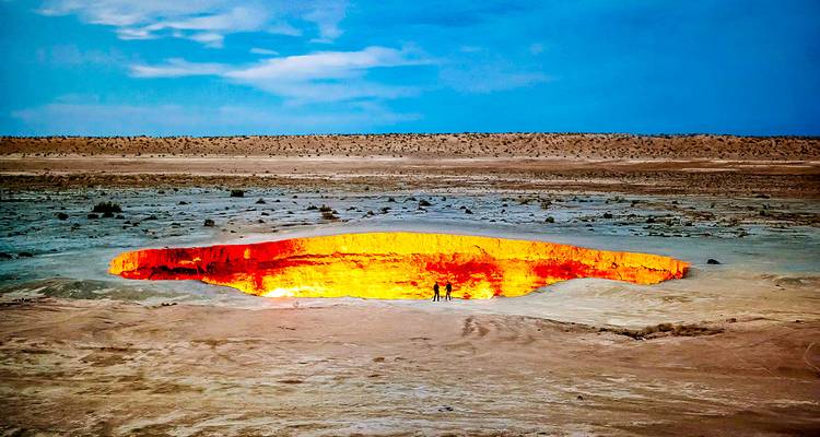 Cráter de gas ardiente de Darvaza brillando al atardecer con pequeñas siluetas de visitantes en el borde