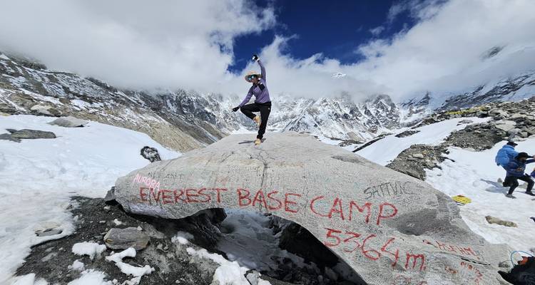 Voyageur pose triomphalement sur un rocher du camp de base de l'Everest avec marquage d'altitude entouré de montagnes enneigées