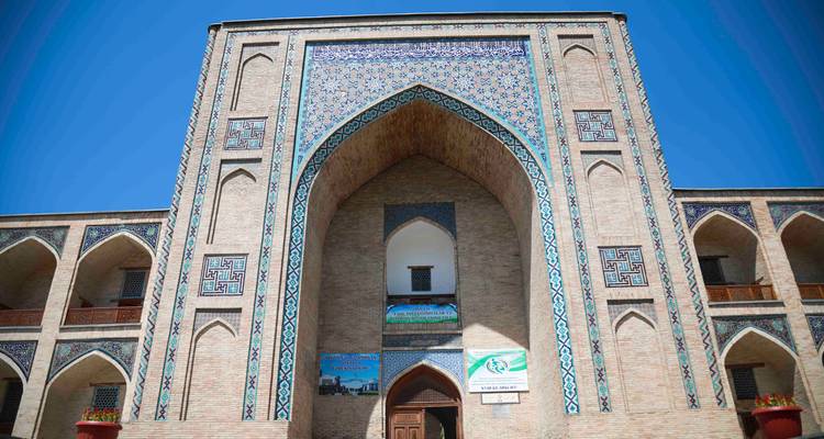 Portail impressionnant d'une madrasa carrelée avec des motifs de mosaïque bleue complexes se détachant sur un ciel bleu profond
