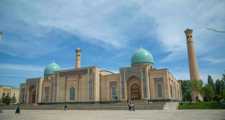 Vue large d'une mosquée avec des minarets jumeaux et des dômes turquoise sous un ciel bleu éclatant, des visiteurs devant