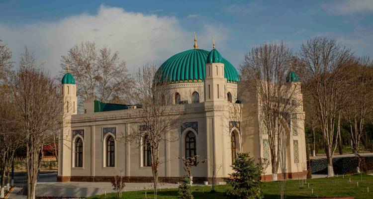 Petit mausolée couleur crème avec des dômes vert vif entouré d'arbres dénudés dans la lumière du début du printemps