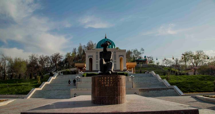 Statue sur un podium menant à un mausolée à dôme au sommet de terrasses paysagères avec des visiteurs gravissant les marches