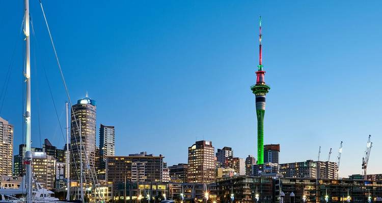 Auckland skyline met verlichte Sky Tower die boven de waterkant uittorent bij schemering.