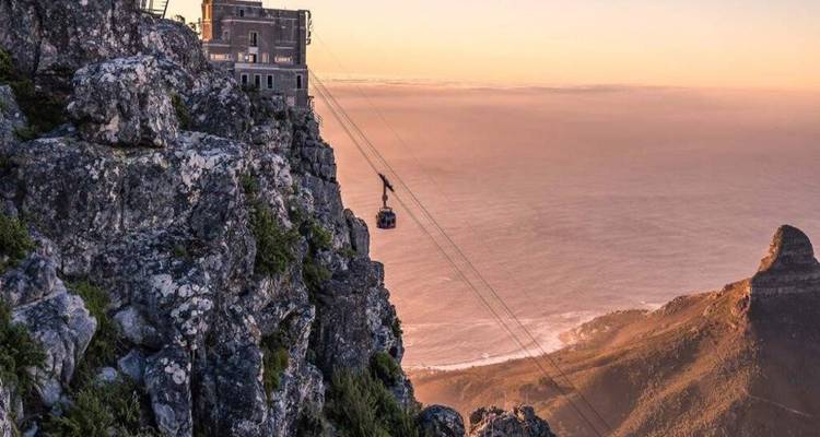 Cable car ascends sheer cliffs of Table Mountain at sunset with golden ocean horizon beyond.