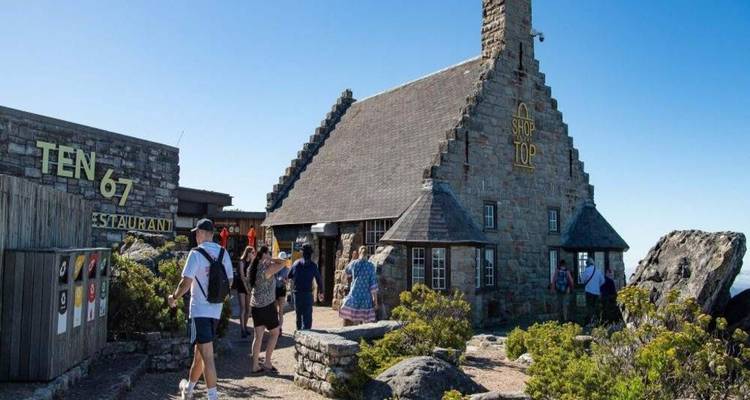 Visitors wander around a stone summit café on Table Mountain under clear blue skies.