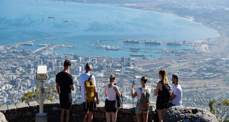 Group of friends enjoy panoramic views of Cape Town harbor from a rocky viewpoint telescope.