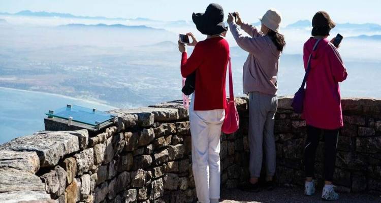 Travelers photograph misty coastal views from a stone parapet high on Table Mountain.