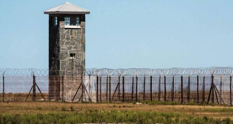 Isolated stone guard tower behind barbed-wire fences on the open grounds of Robben Island prison.