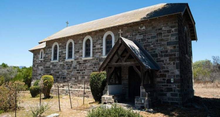 Small stone church with arched windows set in a dry rural landscape under a clear blue sky