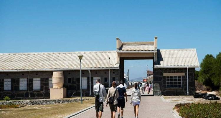 Visitors walking toward the entrance gate of a historic stone prison complex on a bright day