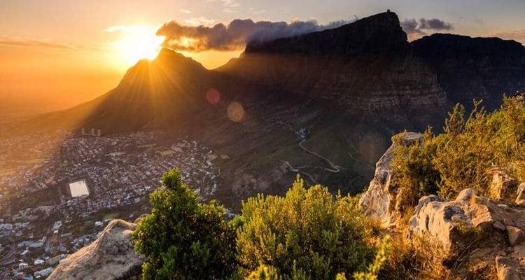 Golden sunset over Table Mountain and Cape Town with dramatic sun rays and rocky foreground