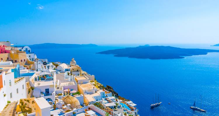 Village emblématique aux maisons blanchies à la chaux perché sur les falaises de Santorin surplombant les eaux bleu profond de la caldeira avec des voiliers.