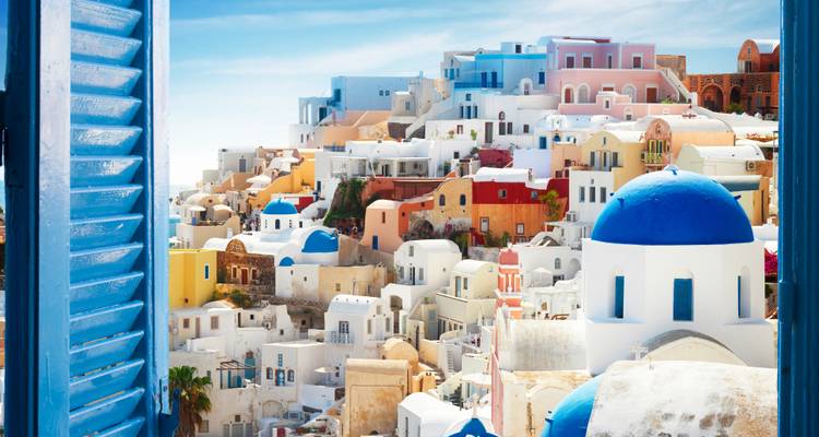 Village de Santorin vu à travers une fenêtre ouverte aux volets bleus mettant en valeur des maisons cubistes colorées et un dôme d'église