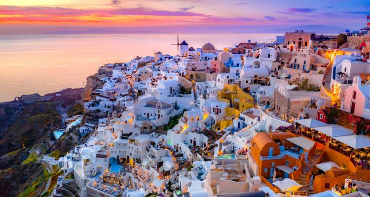Vue aérienne crépusculaire des maisons blanches en cascade de Santorin illuminées contre un ciel de coucher de soleil violet-orange éclatant