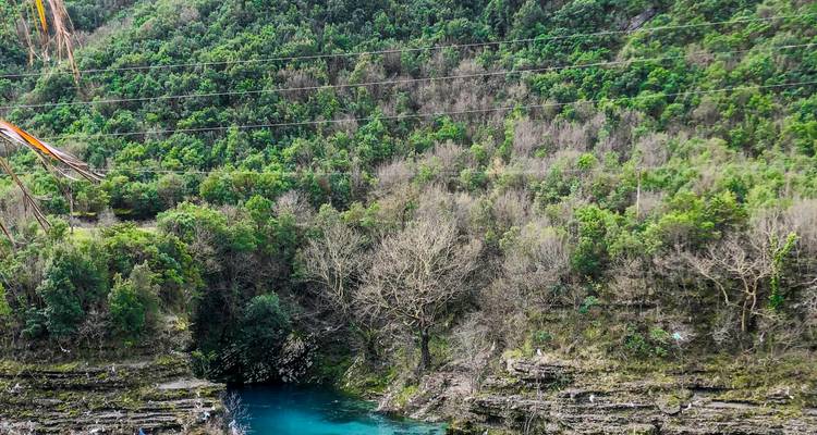 Turquoise rivierkom aan de voet van een steile beboste kloof met hangkabels erboven.