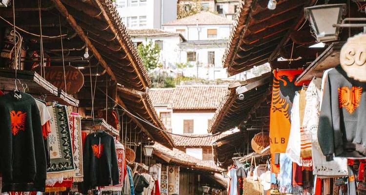 Allée de marché couvert présentant des drapeaux albanais et des vêtements brodés sous des toits de tuiles