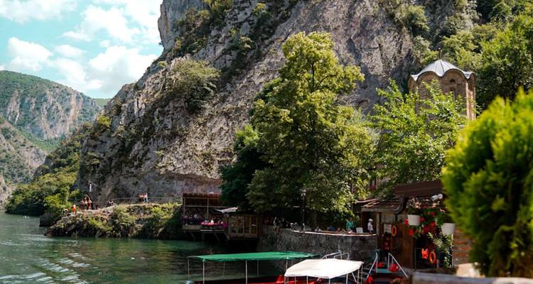 Barcos turísticos amarrados a lo largo de un río esmeralda entre paredes empinadas de cañón con una pequeña iglesia y árboles frondosos.