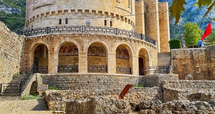 Museo circular de piedra de Skanderbeg dentro del complejo del Castillo de Krujë con balcones arqueados y una bandera albanesa.