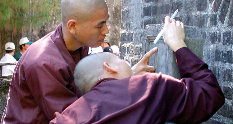 Zwei buddhistische Mönche fertigen Abreibungen von Steininschriften an einer Tempelwand an.