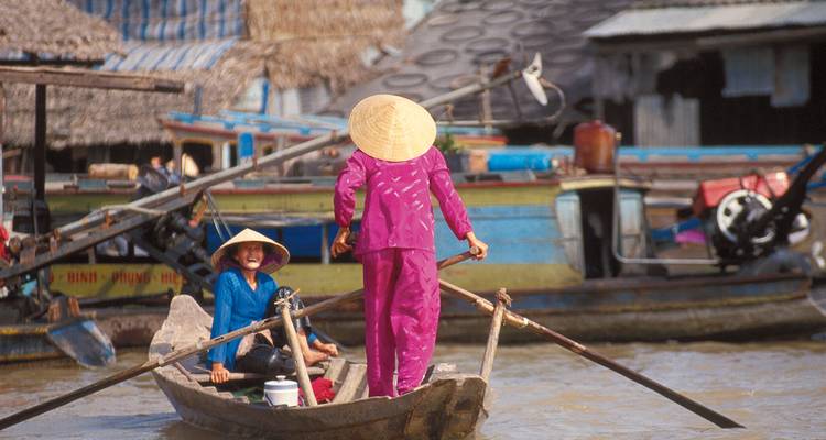 Frauen in heller Kleidung rudern ein Holzboot durch einen geschäftigen schwimmenden Markt im Mekong-Delta.