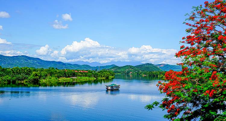 Malerische Bootsfahrt auf dem Parfümfluss inmitten üppiger Hügel und leuchtend roten Blüten.