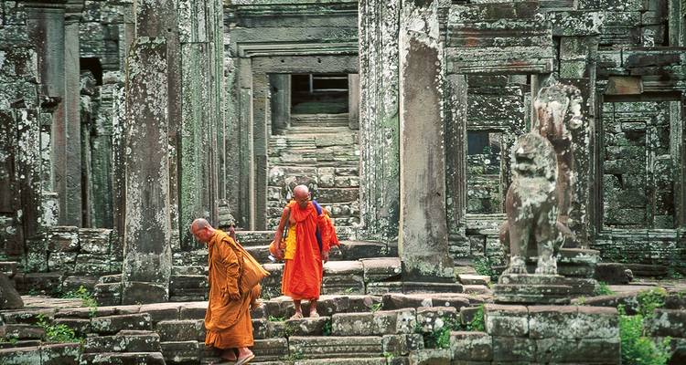 Mönche in orangefarbenen Roben wandeln zwischen den antiken Steinsäulen der Angkor-Ruinen.