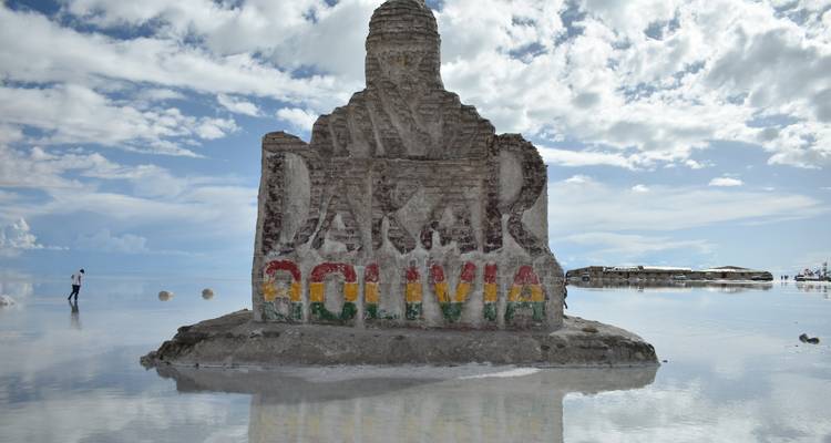 Monumento de piedra Dakar-Bolivia reflejado en las aguas poco profundas del Salar de Uyuni bajo un cielo parcialmente nublado.
