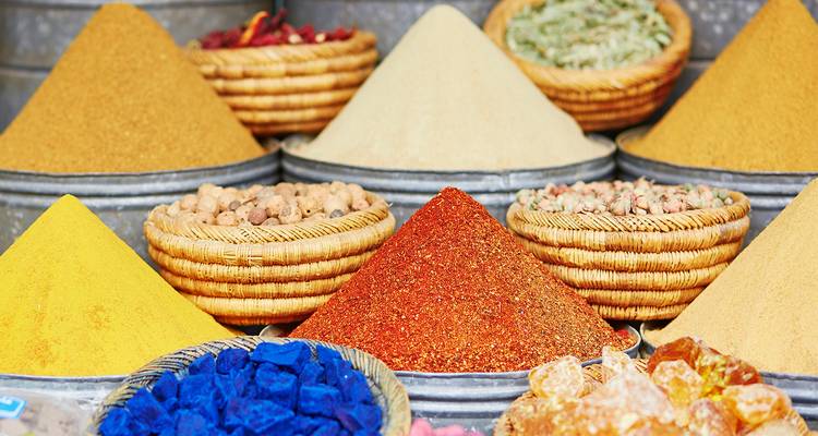 Rows of colorful Moroccan spice pyramids and baskets of herbs at a souk stall.