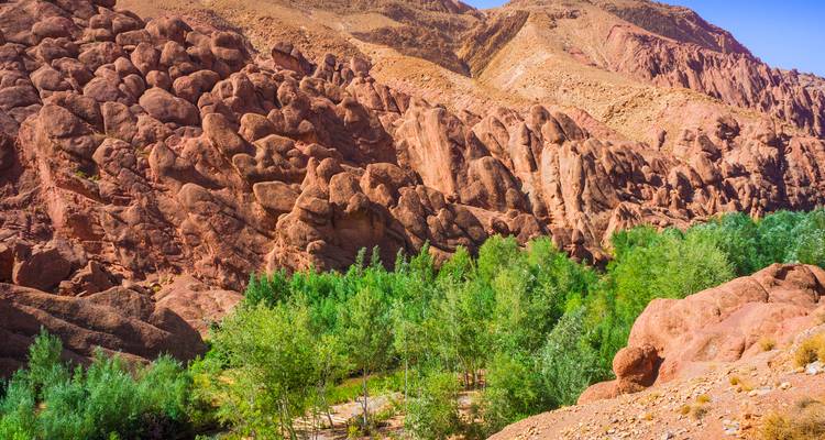 Rugged red rock formations and a ribbon of green oasis trees in the Dades Valley.