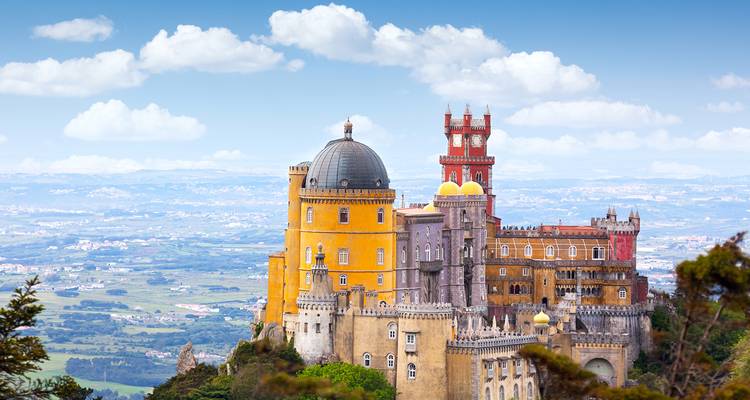 Palais de Pena féerique avec des tours jaunes et rouges perché au sommet d'une montagne boisée à Sintra.