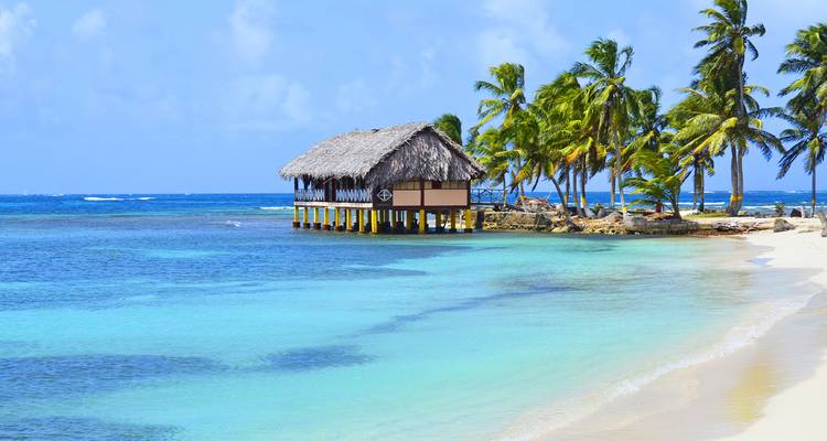 Idyllische Überwasserhütte und palmengesäumter weißer Sandstrand mit türkisfarbenem Wasser auf den San-Blas-Inseln.