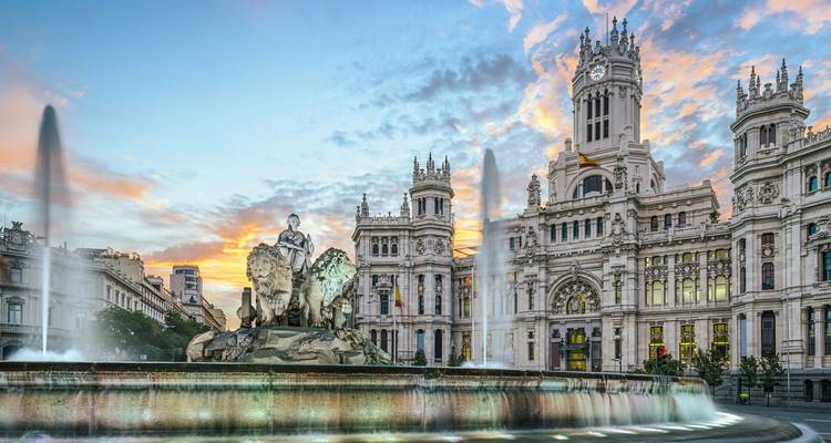 Madrid's Cibeles-fontein en het grandioze Palacio de Cibeles gloeien in warm avondlicht met fonteinen die spuiten tegen een pastelkleurige zonsonderganghemel.